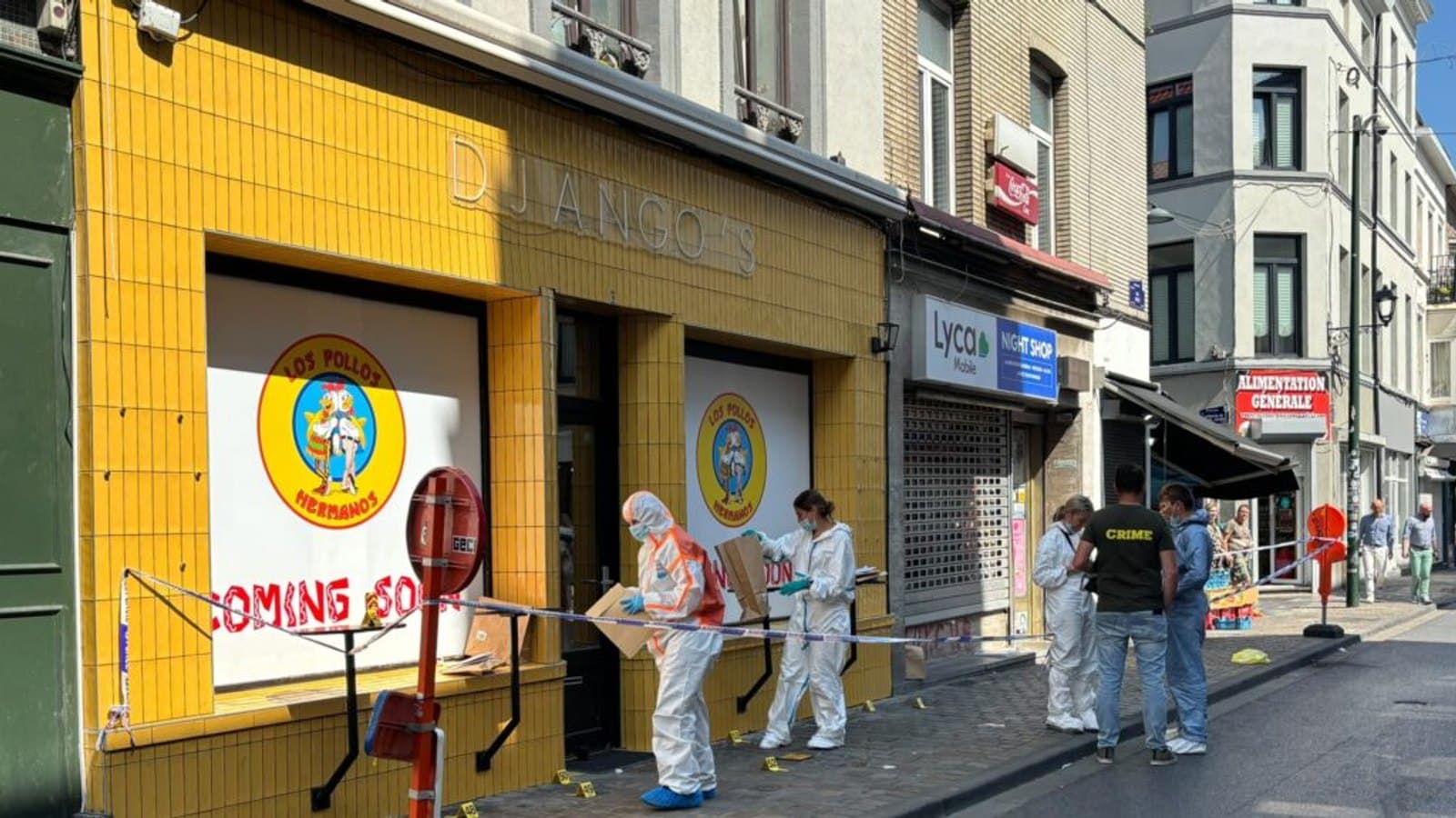 Forensic officers in white suits work behind police tape outside a night shop on a Brussels street, with numbered evidence markers set out on the pavement.