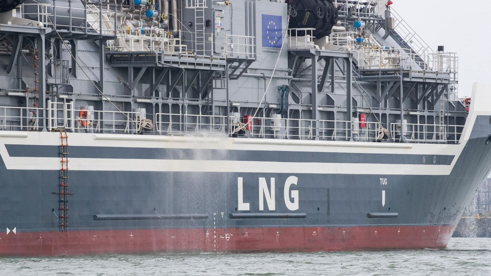 A liquefied natural gas carrier lying alongside, with the letters LNG painted on the hull and a European Union plaque fixed to the superstructure.